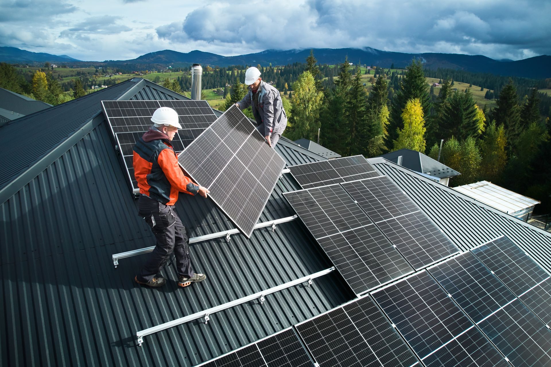 Des ouvriers installent des panneaux solaires sur un toit en pente, avec des montagnes en arrière-plan.