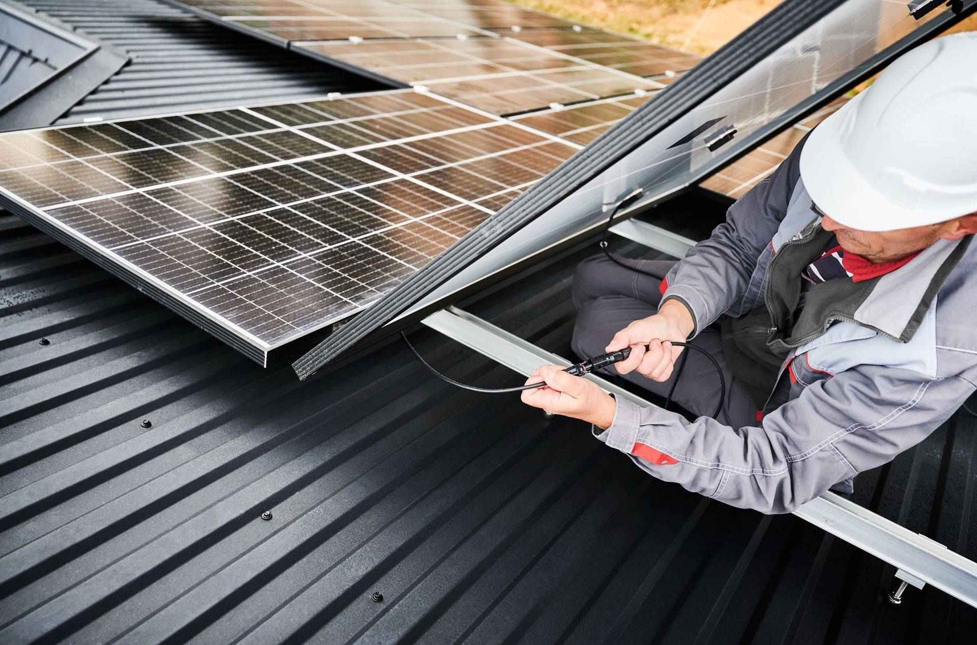 Un ouvrier portant un casque de chantier installe des panneaux solaires sur un toit.