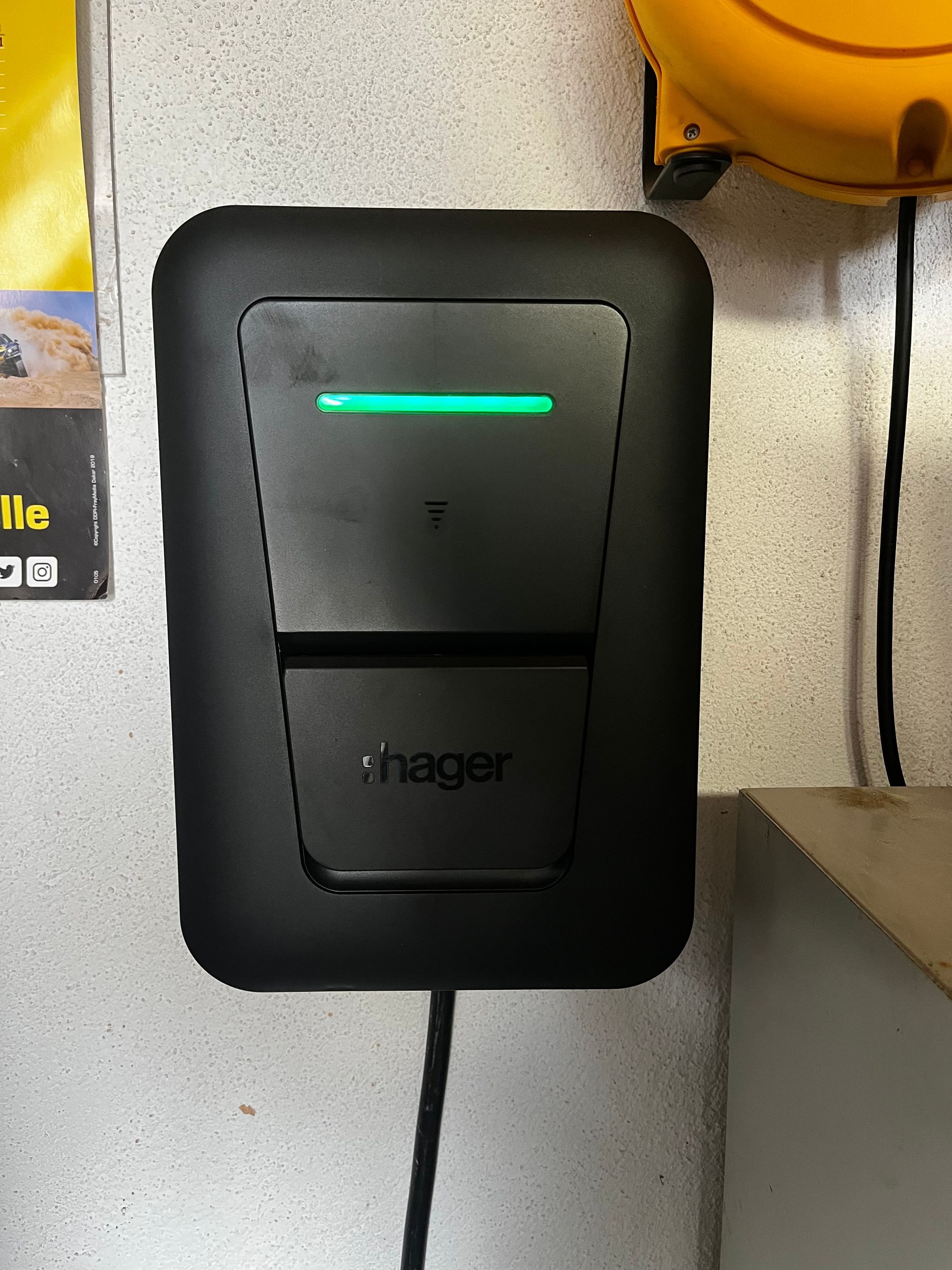 Appareil mural Hager avec voyant vert et câble fixé au mur.