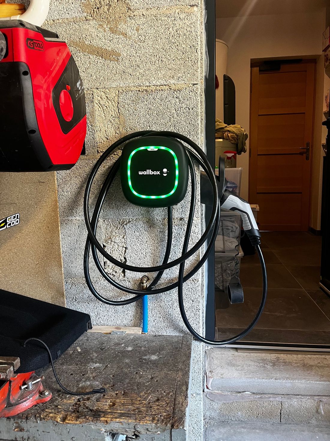 Borne de recharge murale pour véhicules électriques avec écran vert lumineux, fixée sur un mur en pierre.
