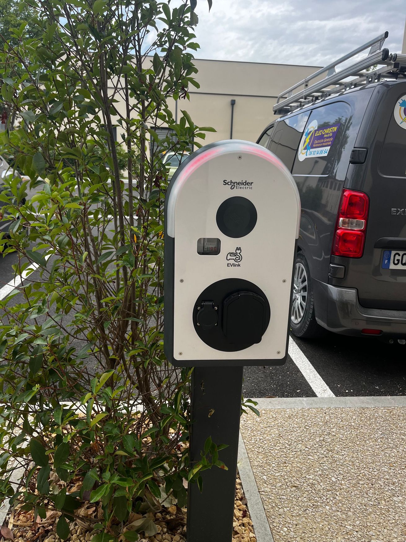 Borne de recharge blanche pour véhicules électriques sur un poteau à côté d'un SUV stationné à l'extérieur.