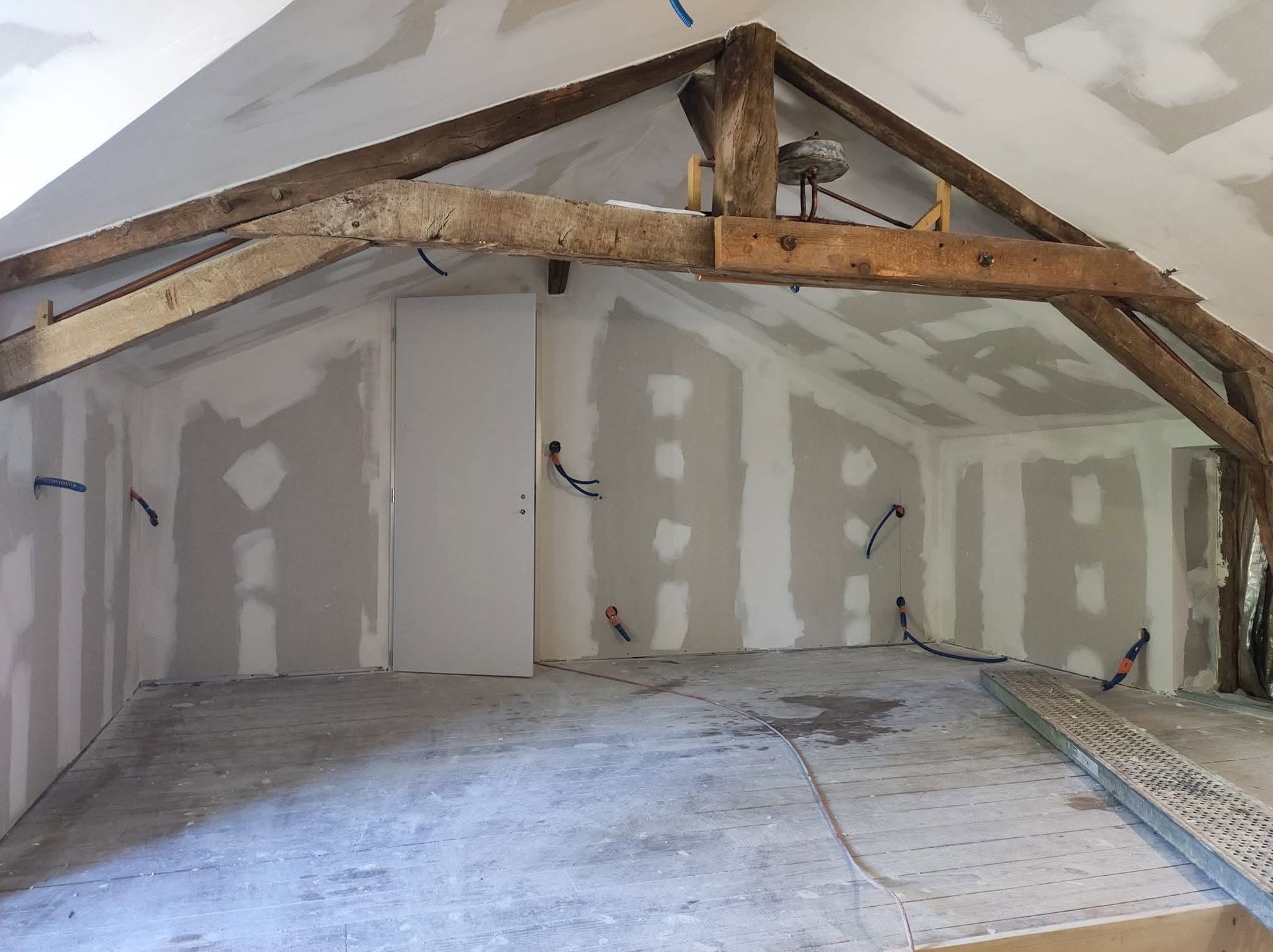 Grenier inachevé avec poutres apparentes, plaques de plâtre réparées et plancher nu.