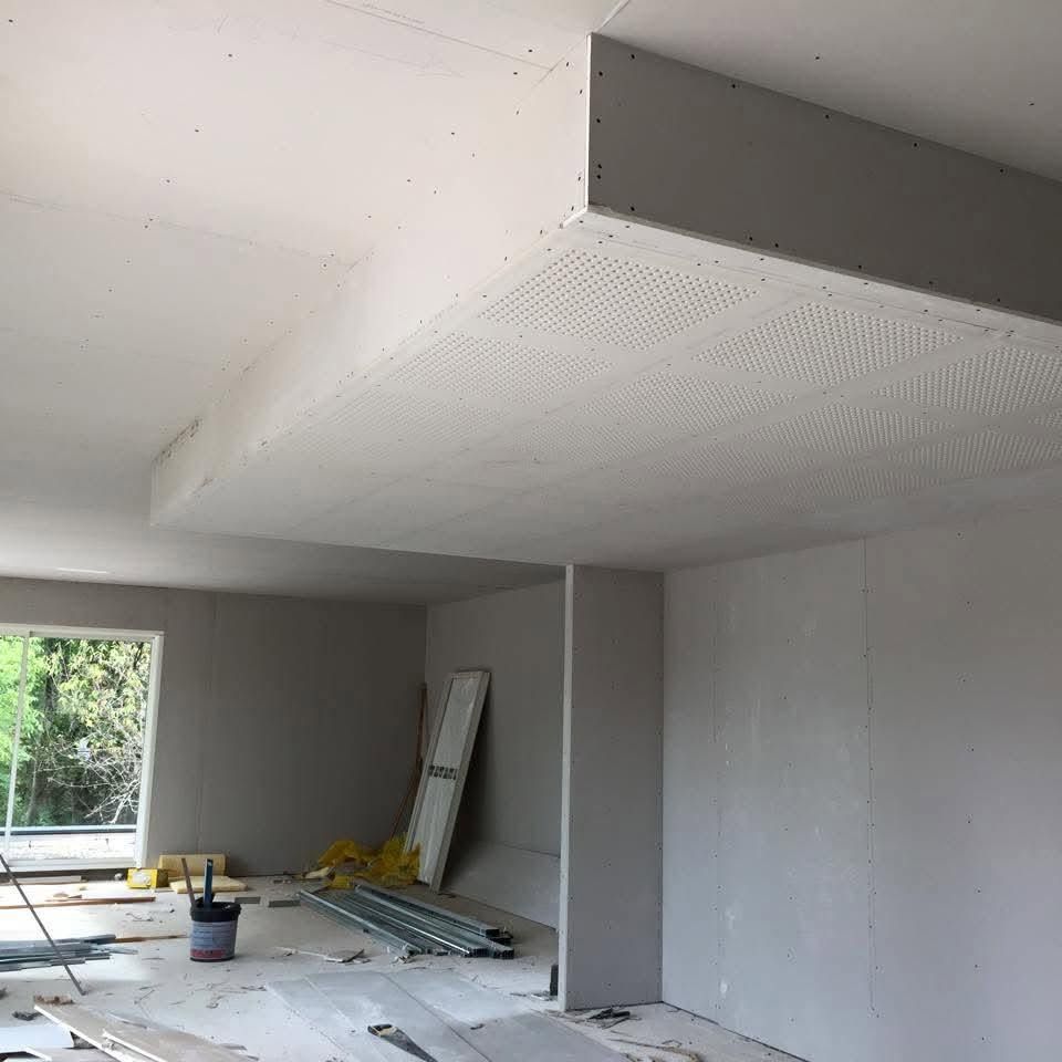 Pièce partiellement aménagée avec murs blancs, poutre apparente au plafond, outils et matériaux au sol près d'une fenêtre.