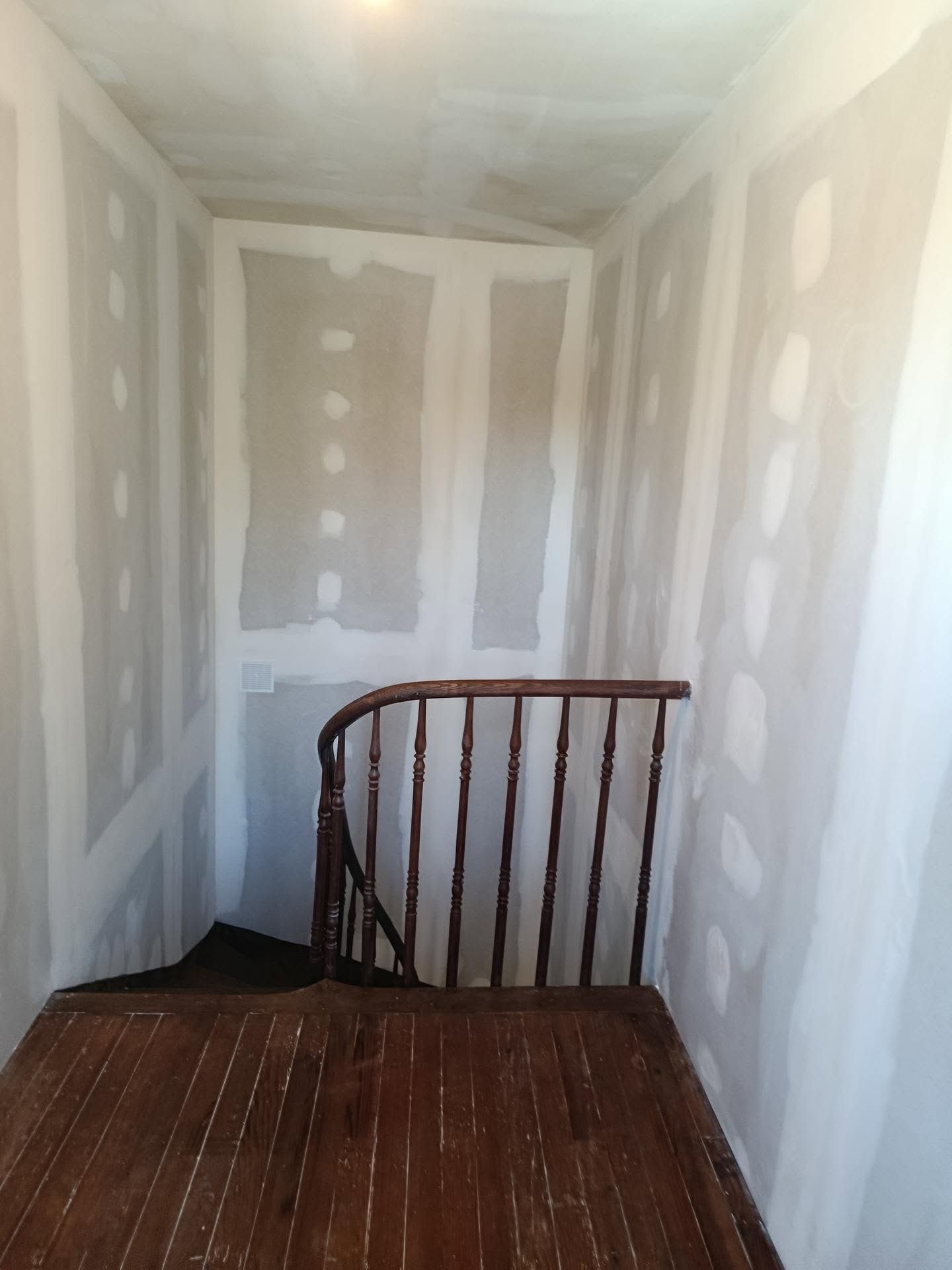 Escalier étroit et inachevé avec cloisons sèches, plancher en bois et rampe sombre.
