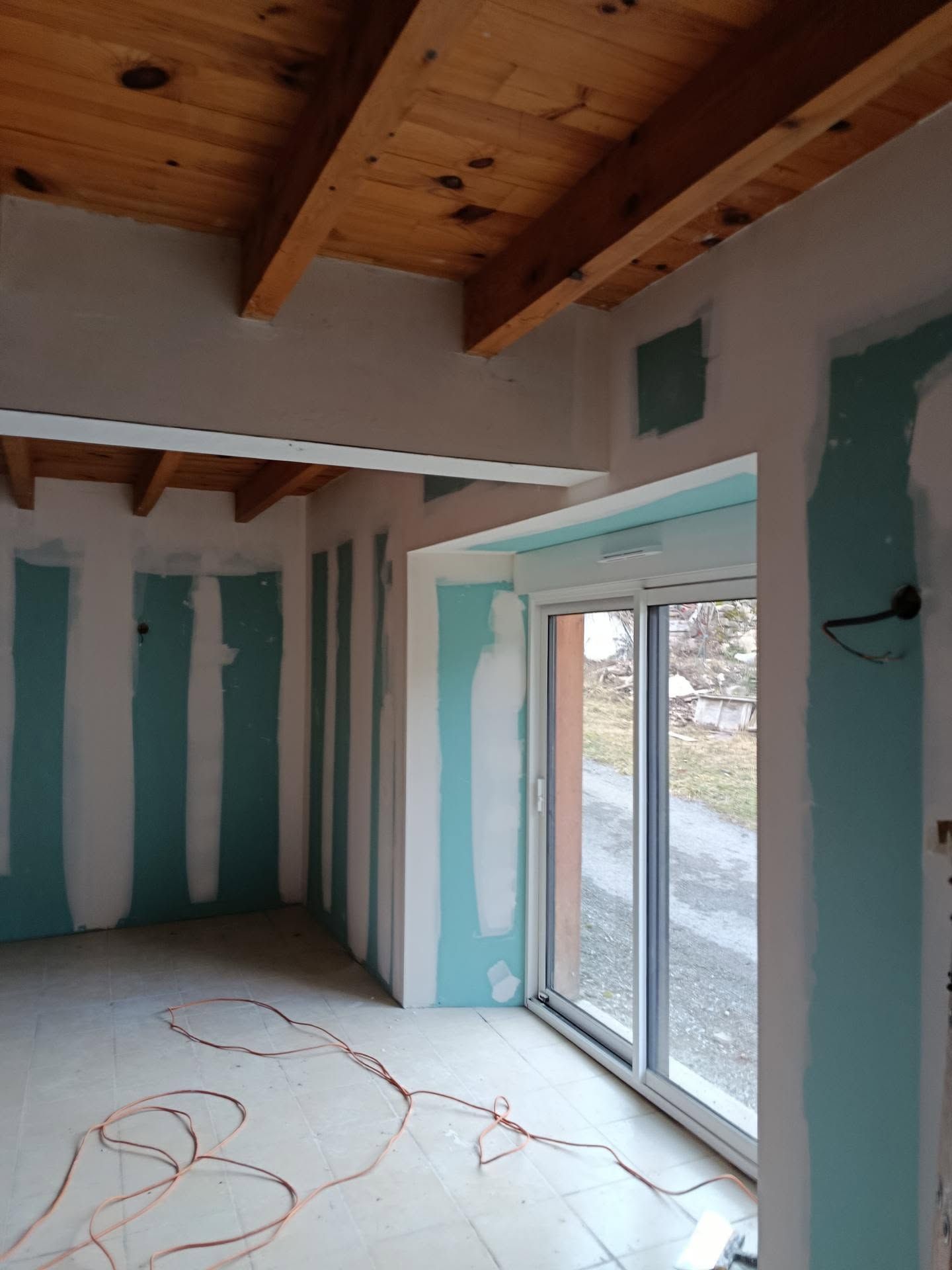 Pièce rénovée avec poutres apparentes, murs à rayures, porte coulissante en verre et câblage au sol non fini.
