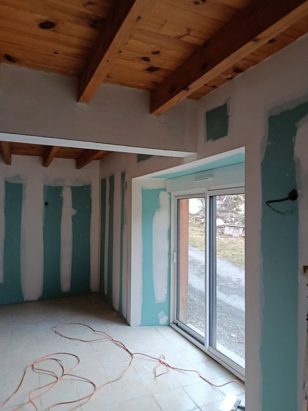 Pièce inachevée avec poutres apparentes, joints de plaques de plâtre collés et portes coulissantes en verre.