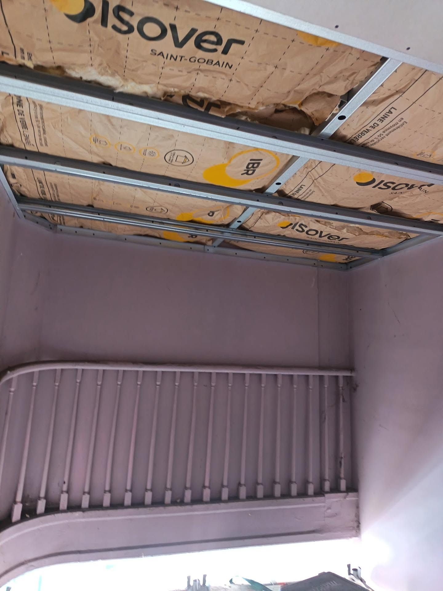 Vue sur le plafond avec isolation apparente et rambarde d'escalier dans un intérieur en travaux.