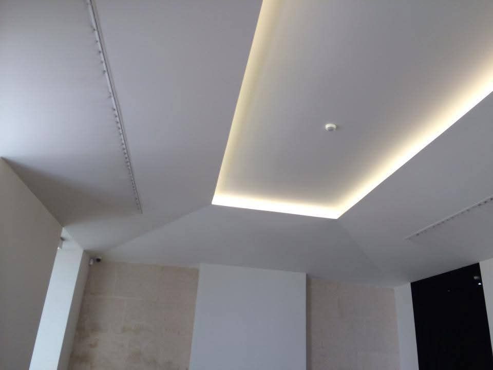Plafond moderne avec éclairage linéaire encastré et murs blancs dans une pièce minimaliste.