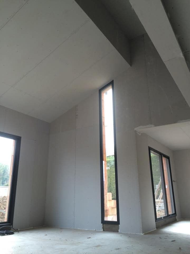Intérieur vide et inachevé avec un haut plafond incliné, de hautes fenêtres étroites et des murs gris.