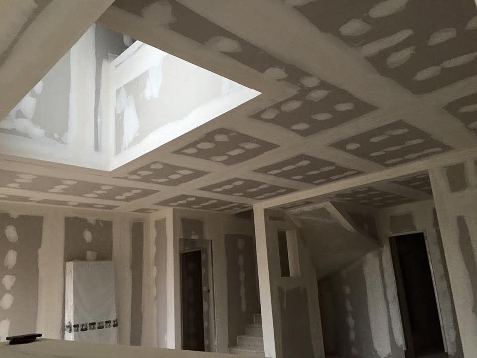 Pièce intérieure en travaux avec des plaques de plâtre réparées et une grande ouverture de puits de lumière.