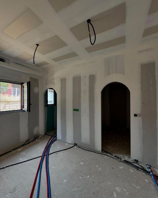 Pièce inachevée avec joints de cloisons sèches, portes cintrées, fenêtre et câbles apparents au sol.