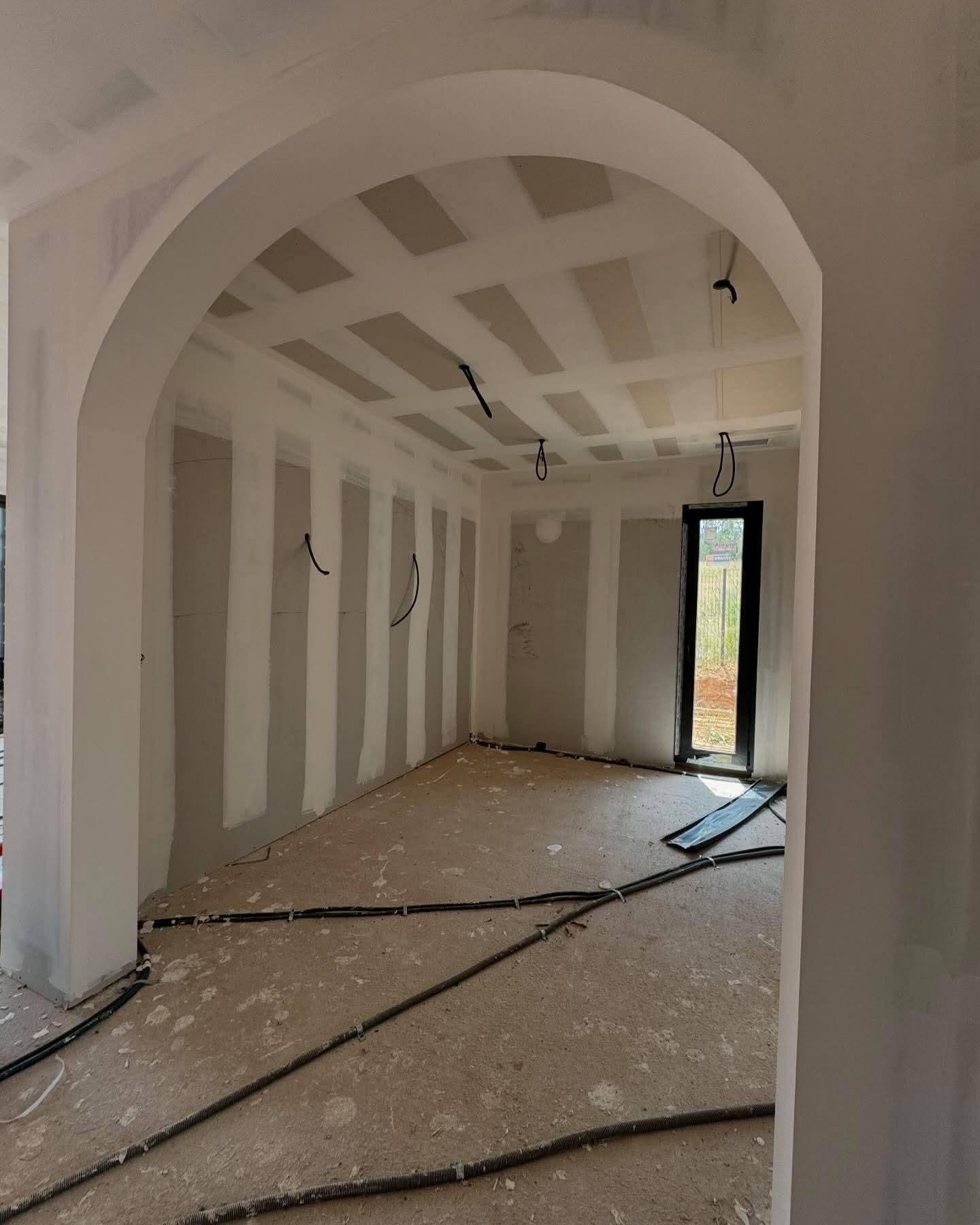 Pièce inachevée avec porte cintrée, poutres apparentes au plafond et débris au sol.