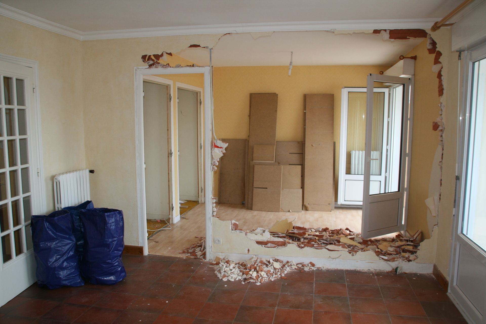 Pièce en rénovation avec ossature murale apparente, débris éparpillés et cartons empilés.