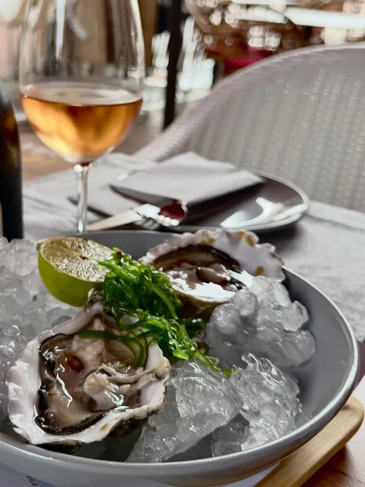 Ostras sobre hielo picado con una rodaja de limón y una copa de vino en una mesa de restaurante.
