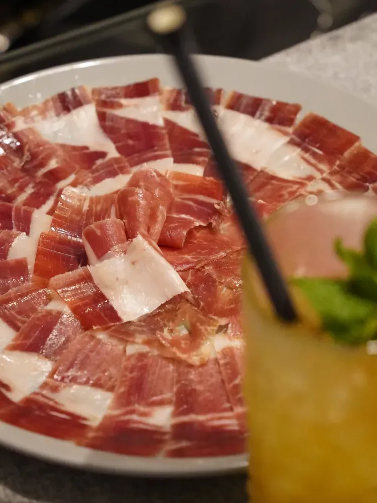 Platos de jamón curado cortado en lonchas finas dispuestos sobre una mesa de restaurante, con una bebida en primer plano.