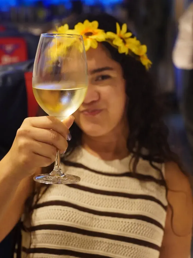 Mujer con blusa de rayas y corona de flores brindando con una copa de vino blanco en el interior.