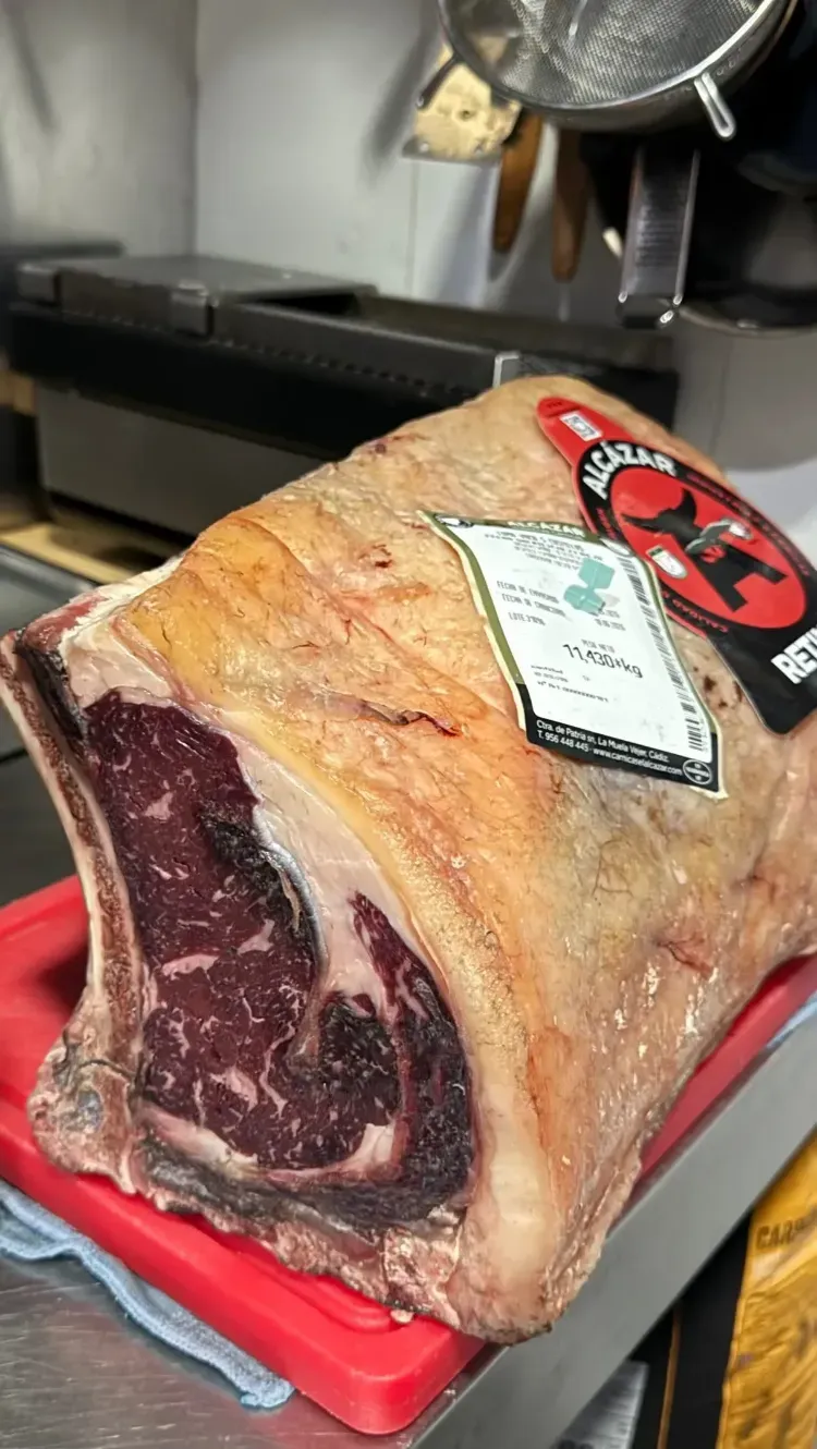 Un trozo grande de carne curada en una bandeja roja con una etiqueta sobre una encimera.