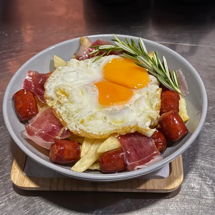 Salchicha, jamón, patatas fritas y un huevo frito con romero en un plato gris.