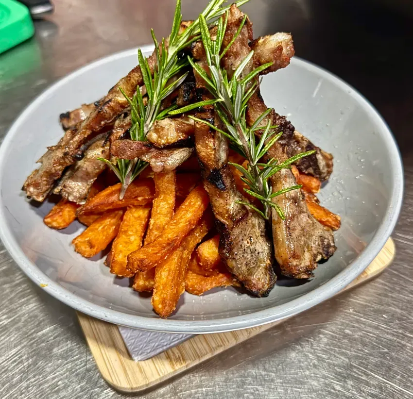 Plato de patatas fritas cubierto con carne a la parrilla y romero sobre una tabla de madera.