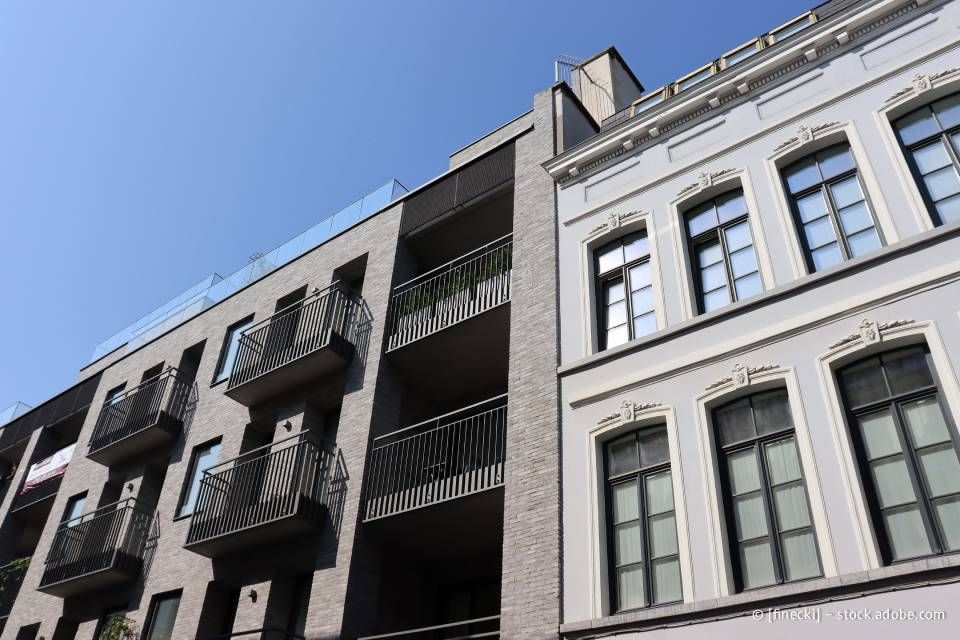 Modernes Wohnhaus neben einem klassischen Gebäude, unter blauem Himmel.