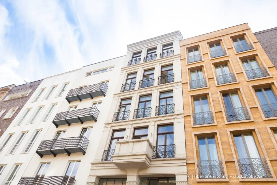Eine Reihe von Wohnhäusern mit unterschiedlich farbigen Fassaden und Balkonen. Blauer Himmel im Hintergrund.