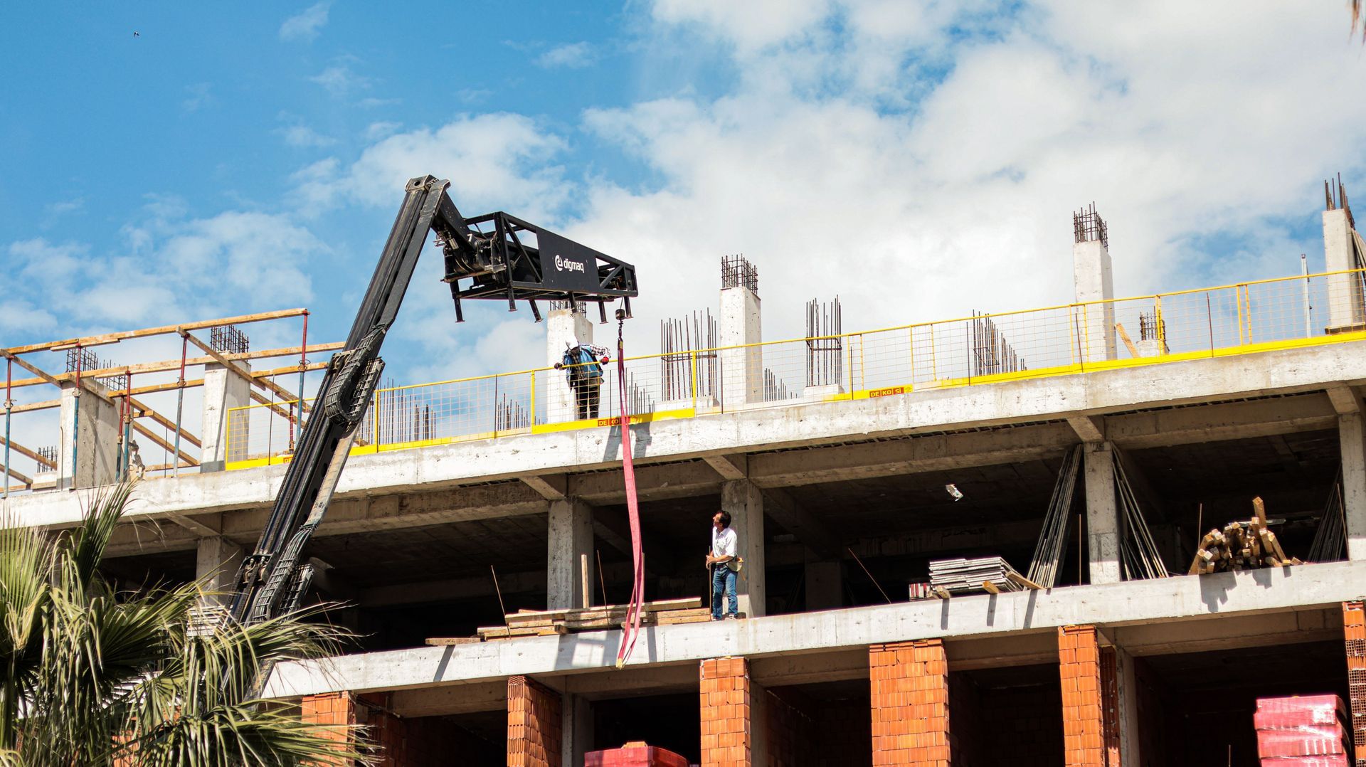 Obra en construcción con una grúa elevando materiales sobre una estructura de hormigón parcialmente construida.