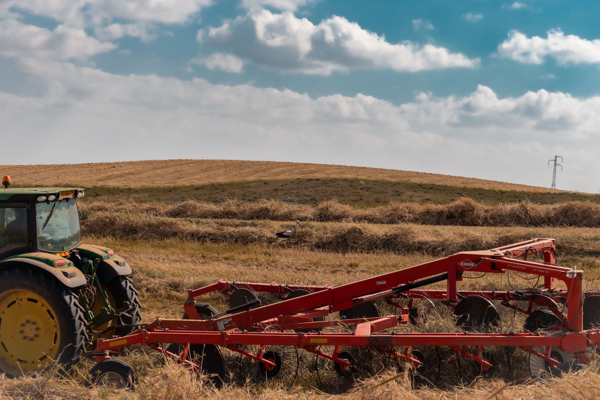 Tractor rojo arrastrando un apero agrícola por un campo seco bajo un cielo nublado