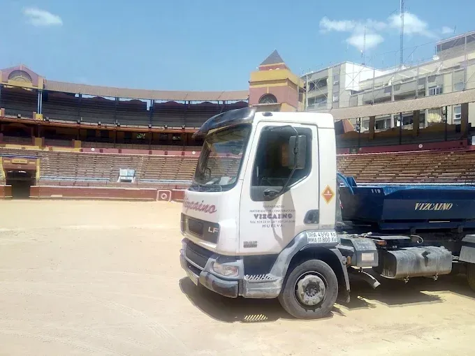 Camión volquete blanco estacionado en una arena deportiva bajo un cielo despejado