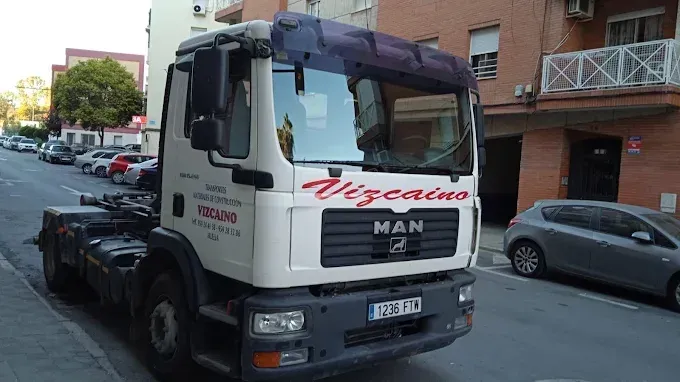 Camión de carga MAN blanco aparcado en una calle de la ciudad, junto a edificios de ladrillo y coches estacionados