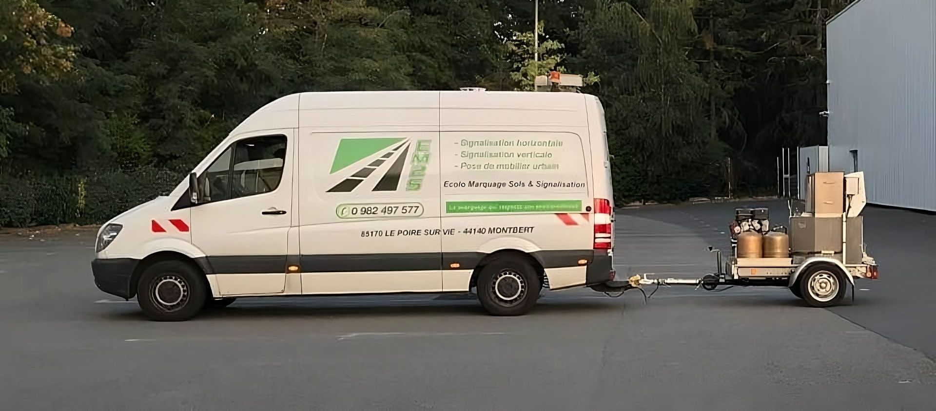 Fourgonnette de service blanche avec logo et texte verts, tractant une petite remorque chargée de matériel sur un parking.