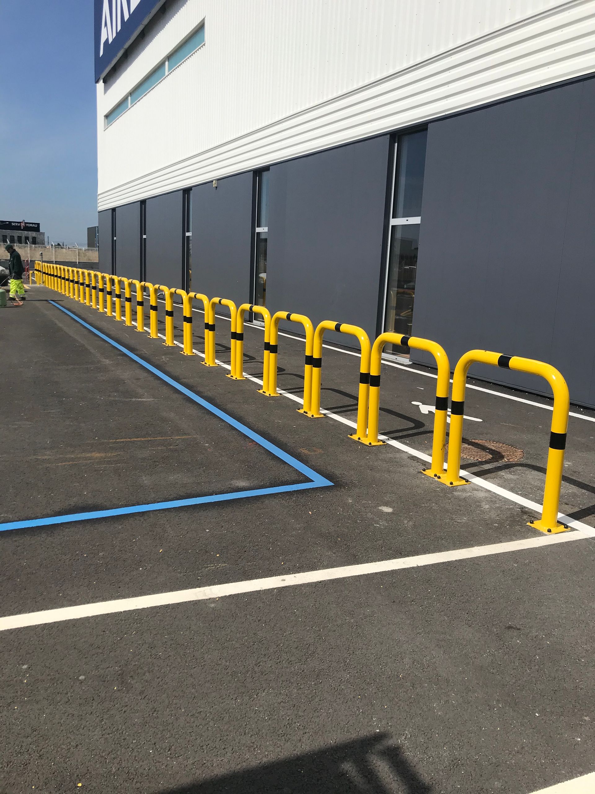 Une longue rangée de bornes de sécurité en métal jaune installées le long du bord d'un bâtiment et d'une place de parking.