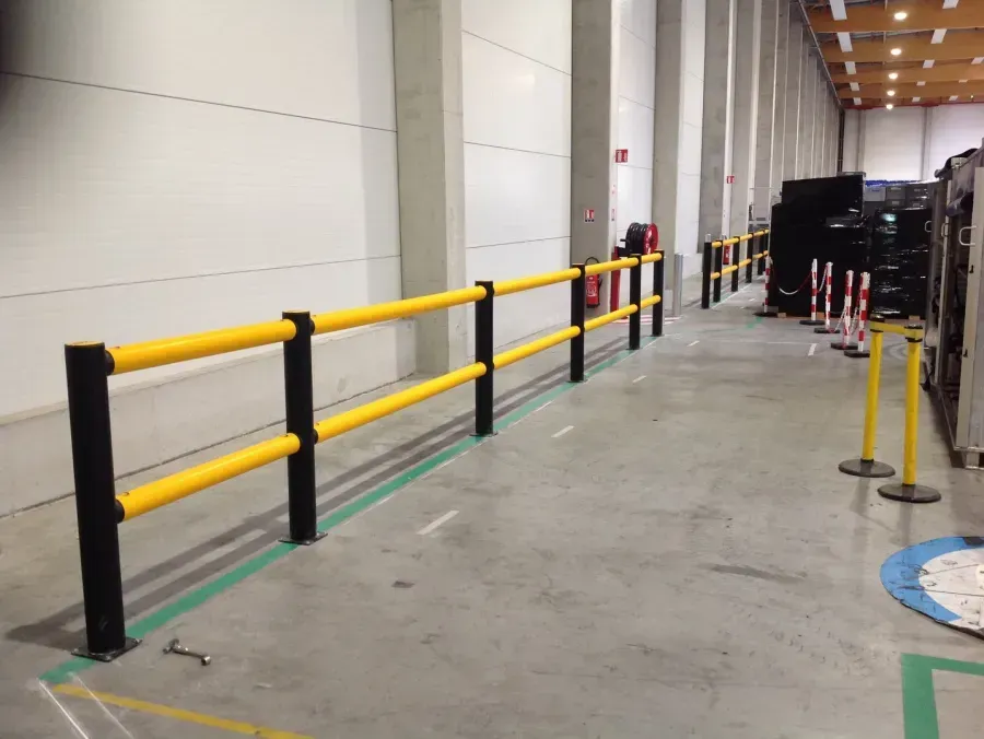 Garde-corps industriels jaunes et noirs installés le long d'un mur d'entrepôt sur un sol en béton.