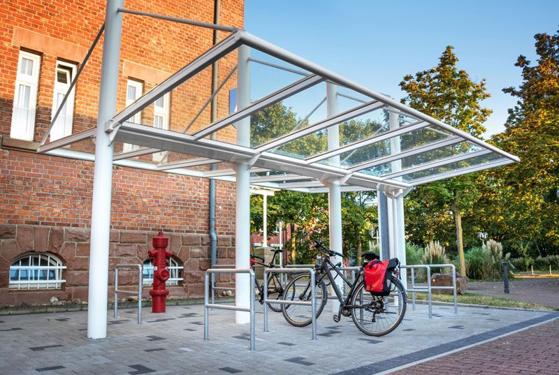 Abri à vélos avec un vélo garé à l'intérieur, près d'un bâtiment en briques.