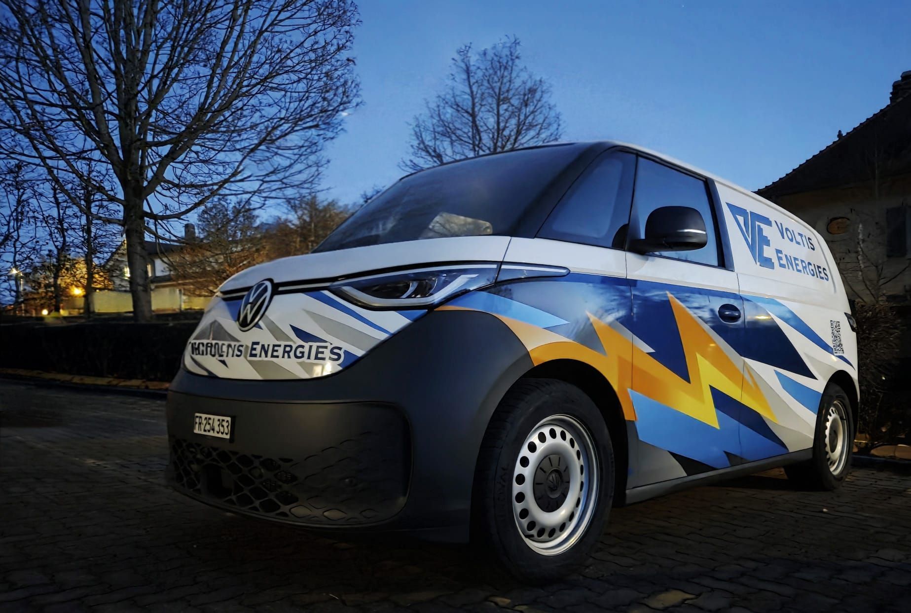 Camionnette blanche avec logo bleu, garée devant le bâtiment.