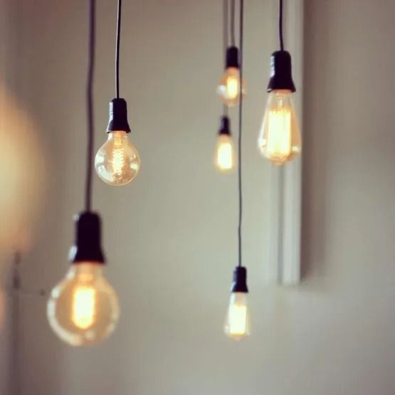 Des ampoules suspendues, à filament lumineux, projettent une lueur chaude sur un mur aux tons neutres.