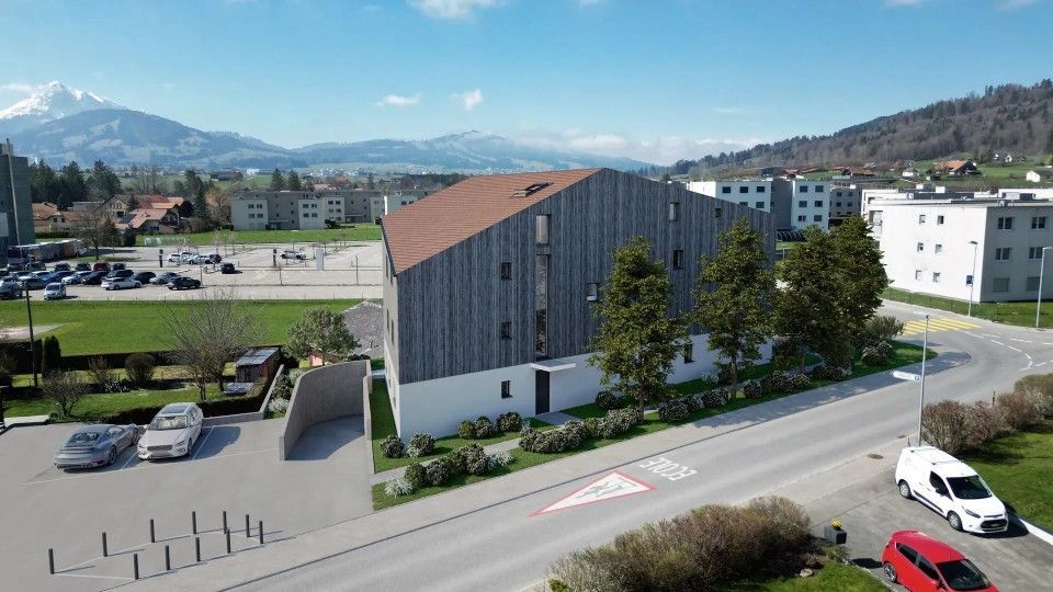Immeuble d'appartements moderne avec bardage en bois brun, soubassement blanc et vue sur les montagnes.