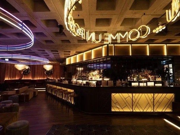 Intérieur de bar avec enseigne lumineuse, bar éclairé et coin salon.