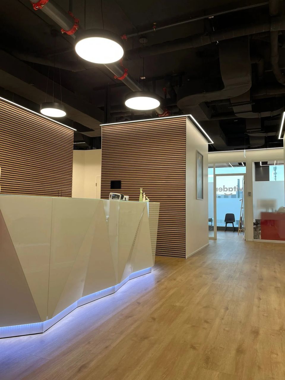 Espace d'accueil moderne avec bureau géométrique blanc, murs lambrissés et éclairage lumineux.