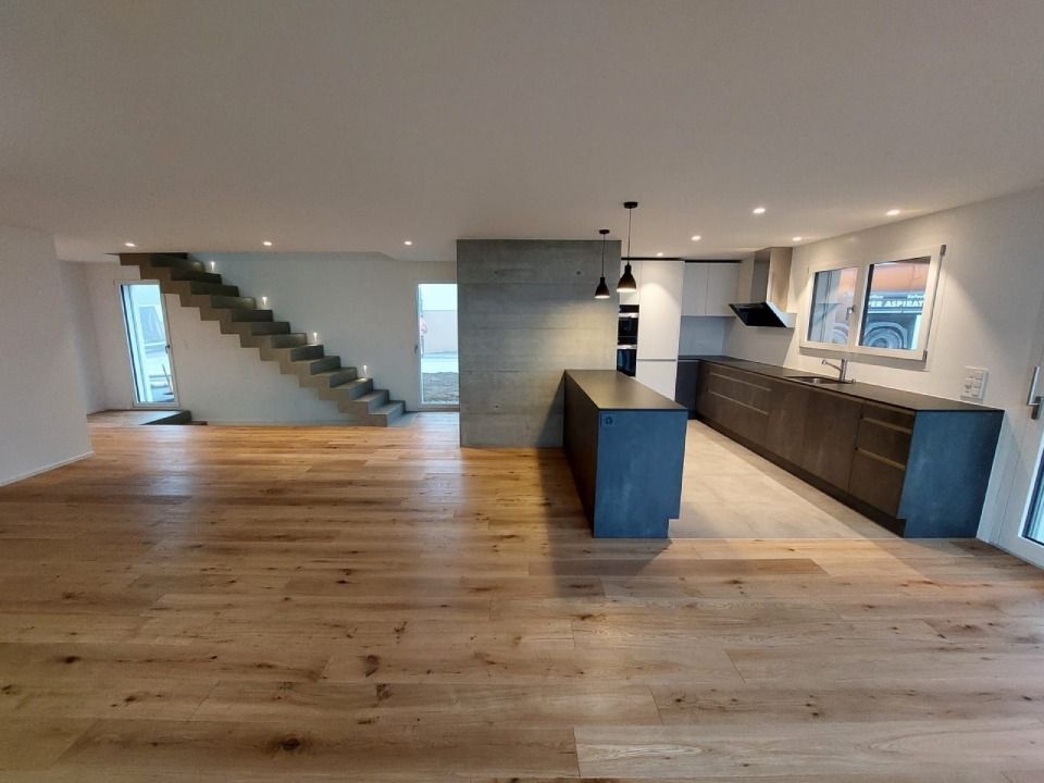 Cuisine moderne avec parquet, îlot central, placards et escalier menant à l'étage.