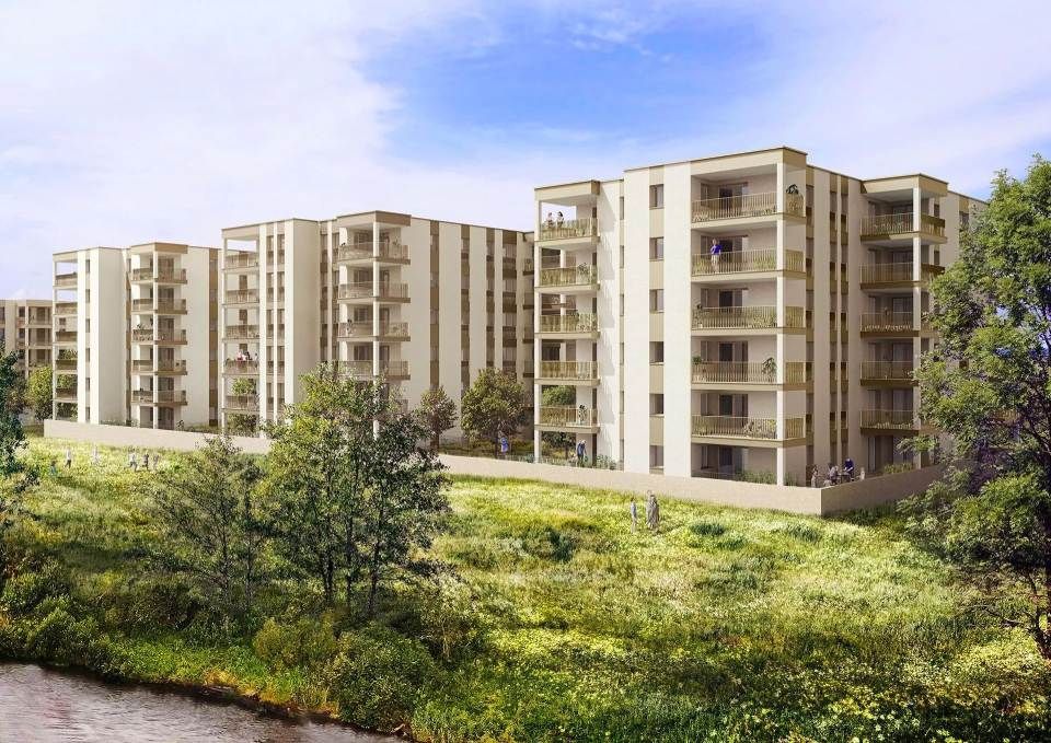 Immeubles d'appartements à plusieurs étages sur une colline herbeuse, vus depuis un cours d'eau sous un ciel.