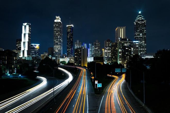 Ville la nuit, avec des traînées lumineuses sur une autoroute sinueuse sous de hauts bâtiments.