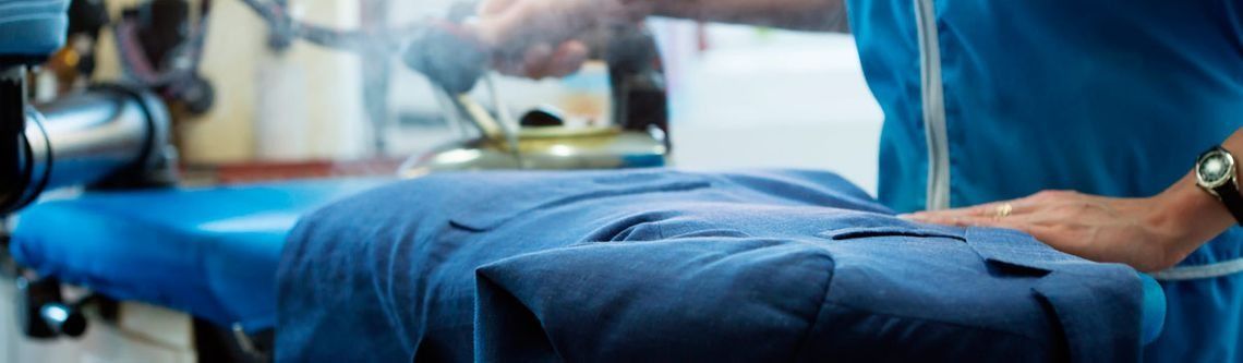 Una persona planchando un blazer azul en una tabla de planchar azul con una plancha de vapor.