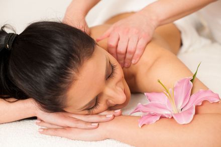 Eine Frau mit einer rosa Blume auf der Schulter bekommt in einem Spa eine Massage.