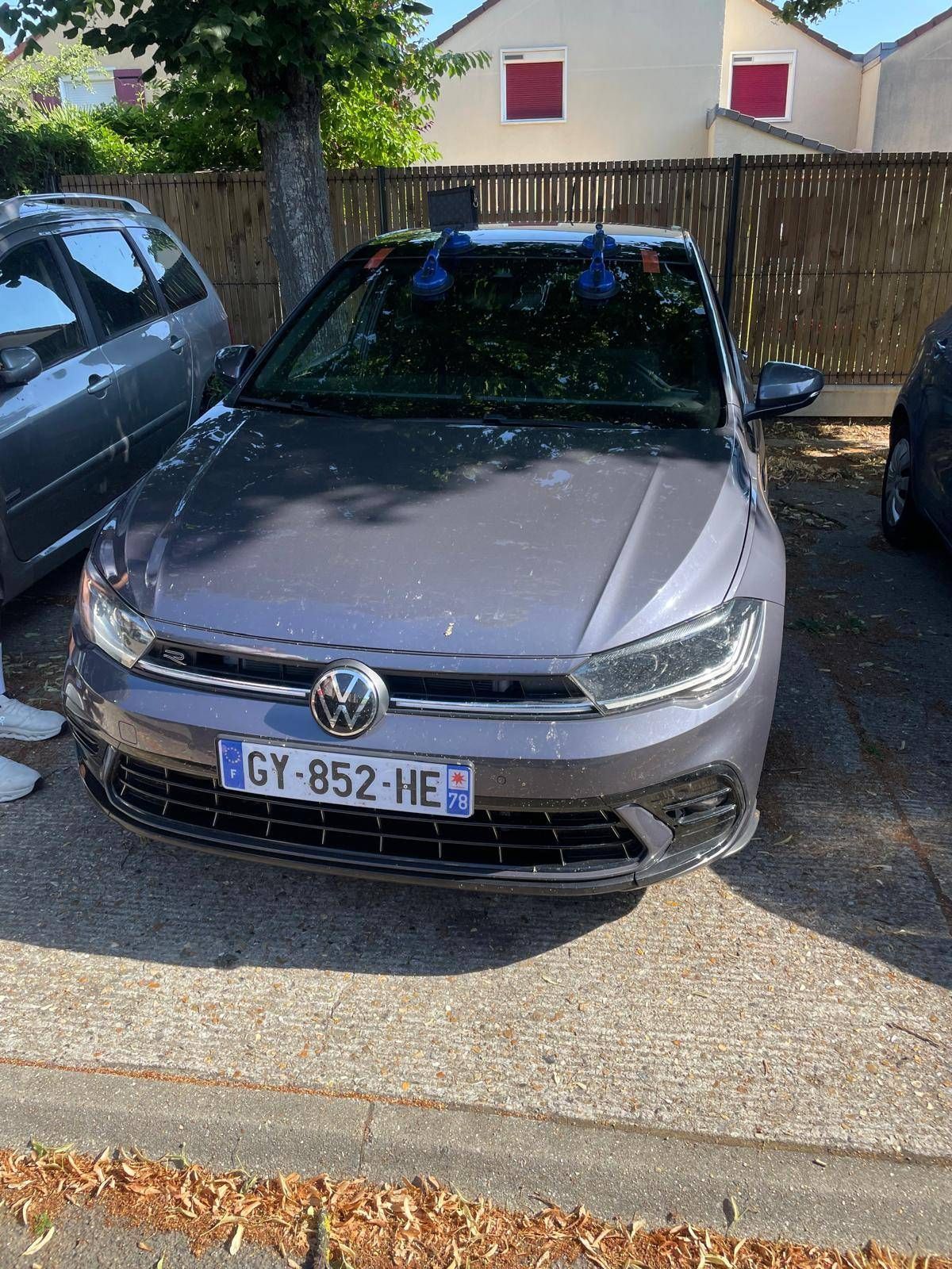 Volkswagen argentée garée dans une rue ensoleillée, à côté d’une autre voiture et d’une clôture