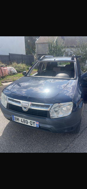 Berline Dacia bleue garée dans une rue ensoleillée, vue de face.