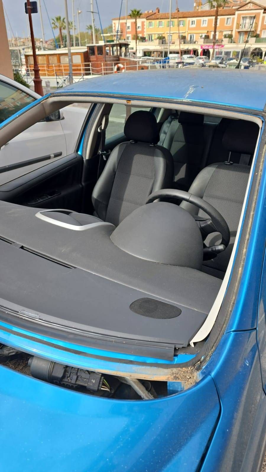Voiture bleue avec le pare-brise avant brisé et le toit endommagé, garée dehors en plein jour