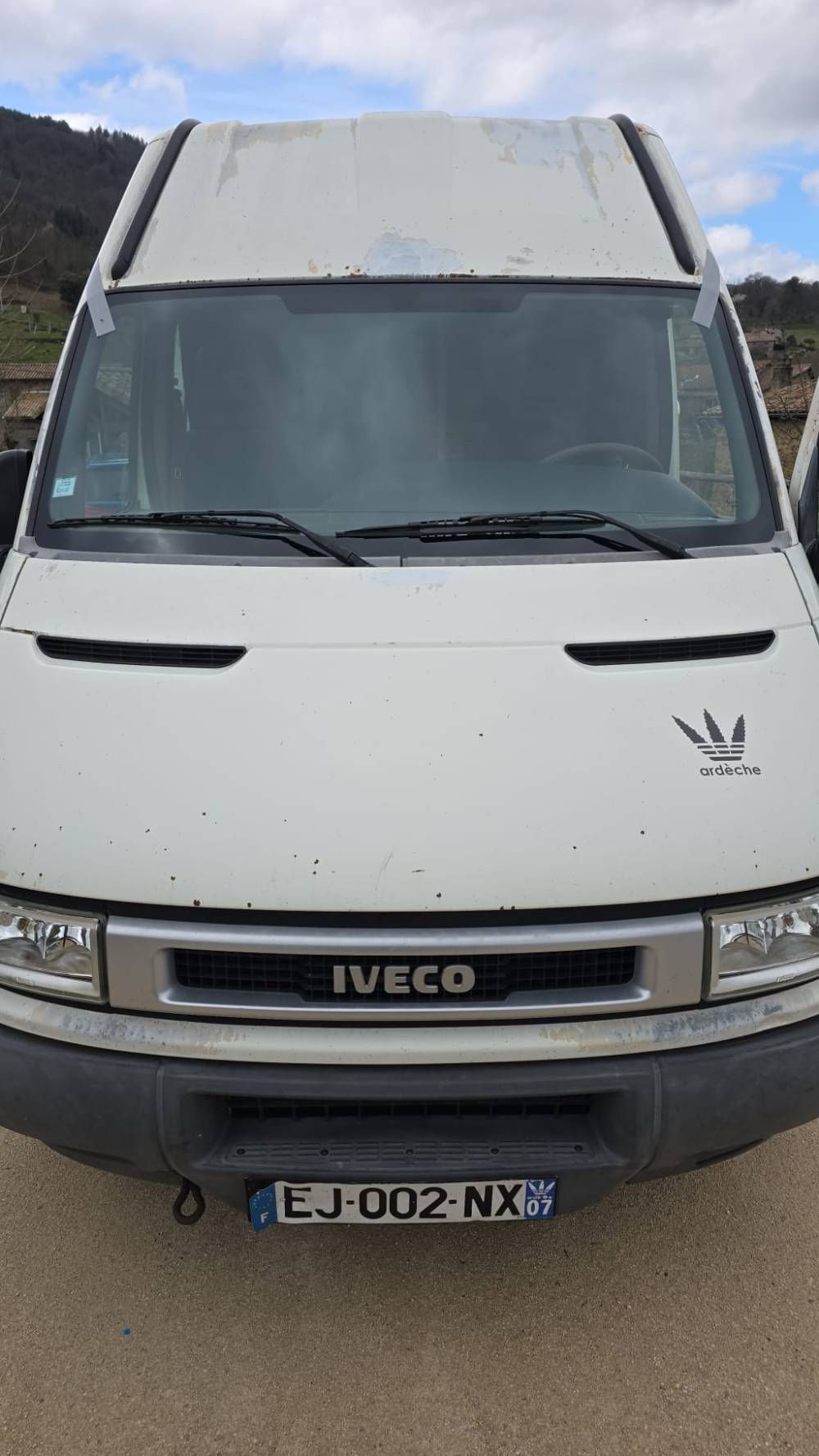 Vue de face d’un fourgon Iveco blanc garé sur une route sous un ciel nuageux.