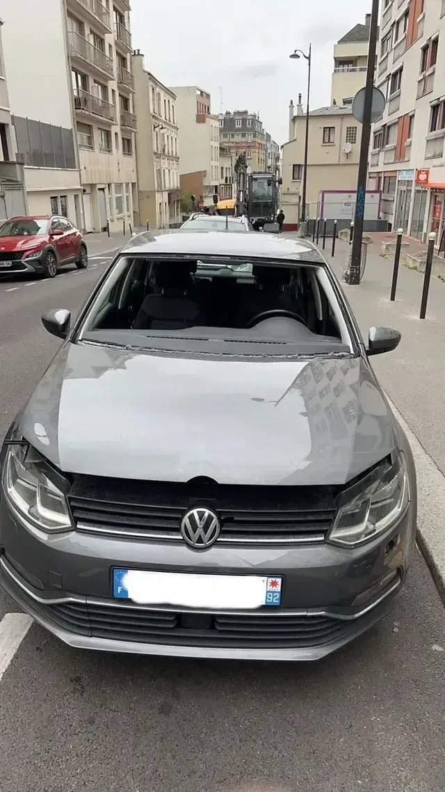 Voiture Volkswagen grise garée dans une rue en ville, entre des immeubles, vue de face