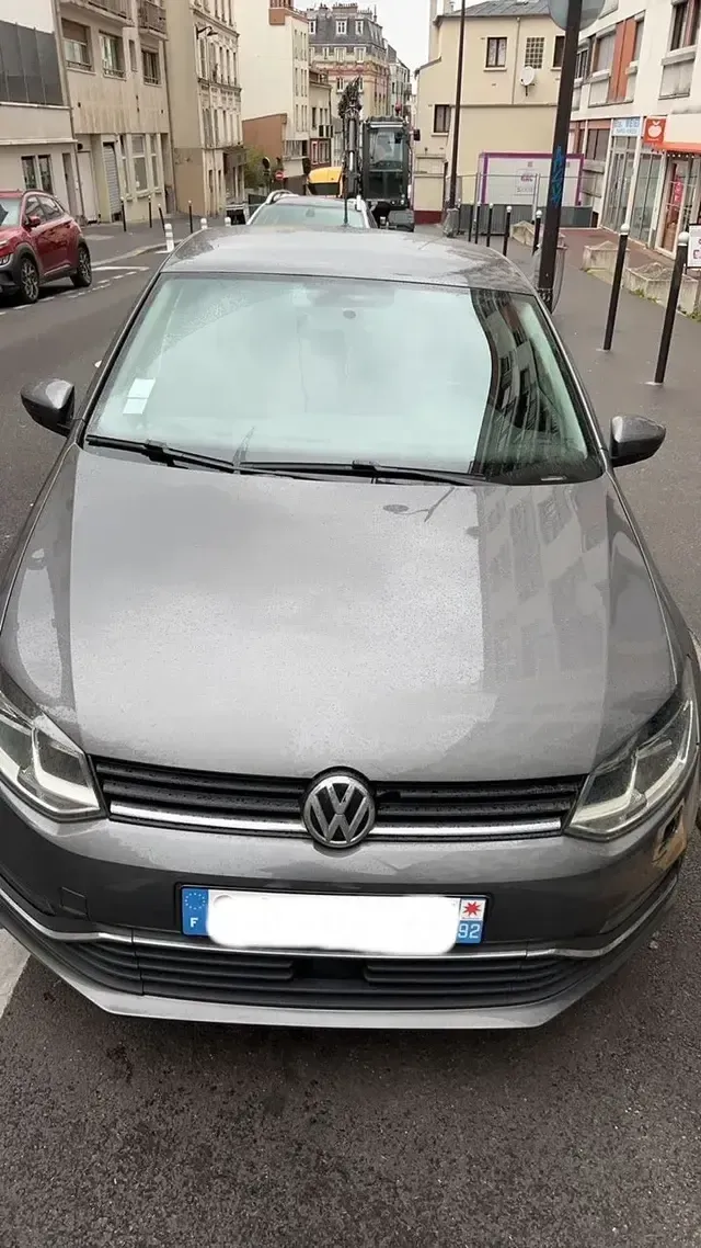 Volkswagen grise stationnée dans une rue étroite en ville, vue de face, chaussée mouillée