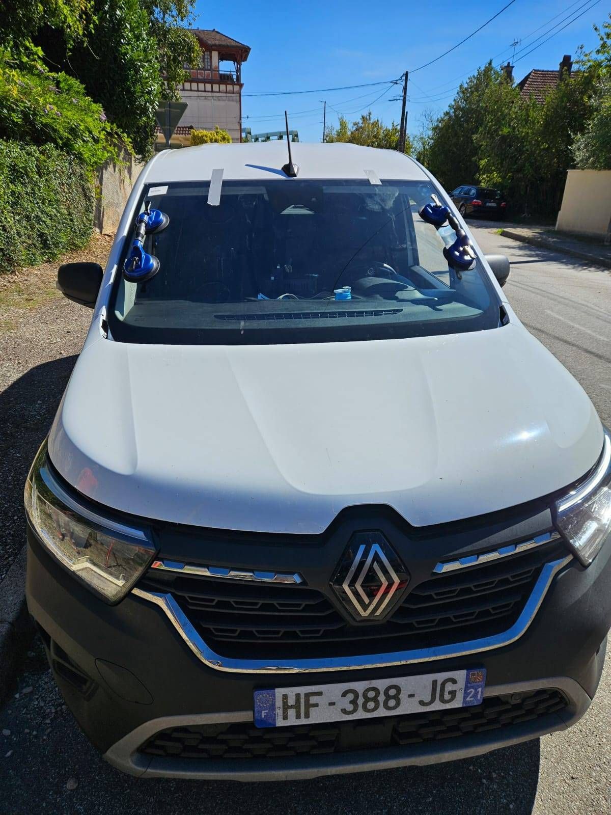 Fourgonnette Renault blanche garée dans une rue ensoleillée, vue de face avec une plaque d’immatriculation visible.